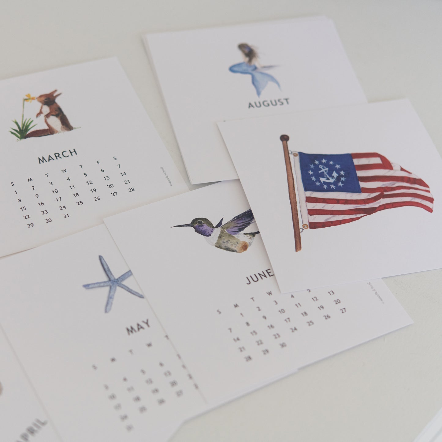 Small calendar with illustrations of a flag, bird, and starfish on a white surface