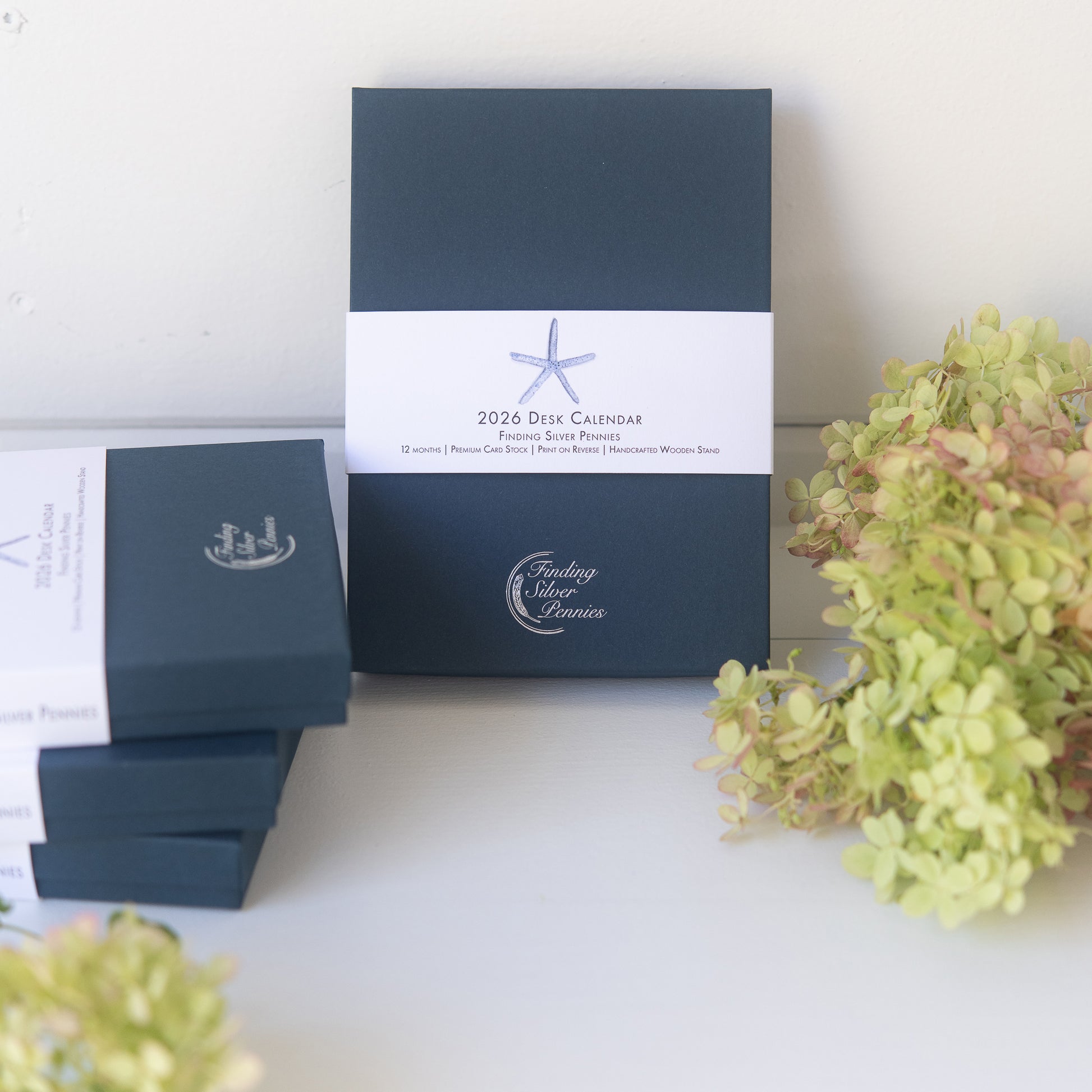 Navy blue desk calendar with white label and decorative flowers on a light surface