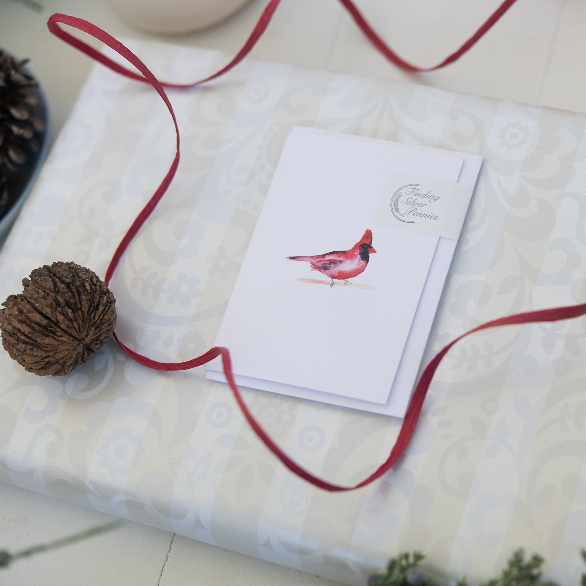 Card with a red bird illustration on a white textured surface with a red ribbon.
