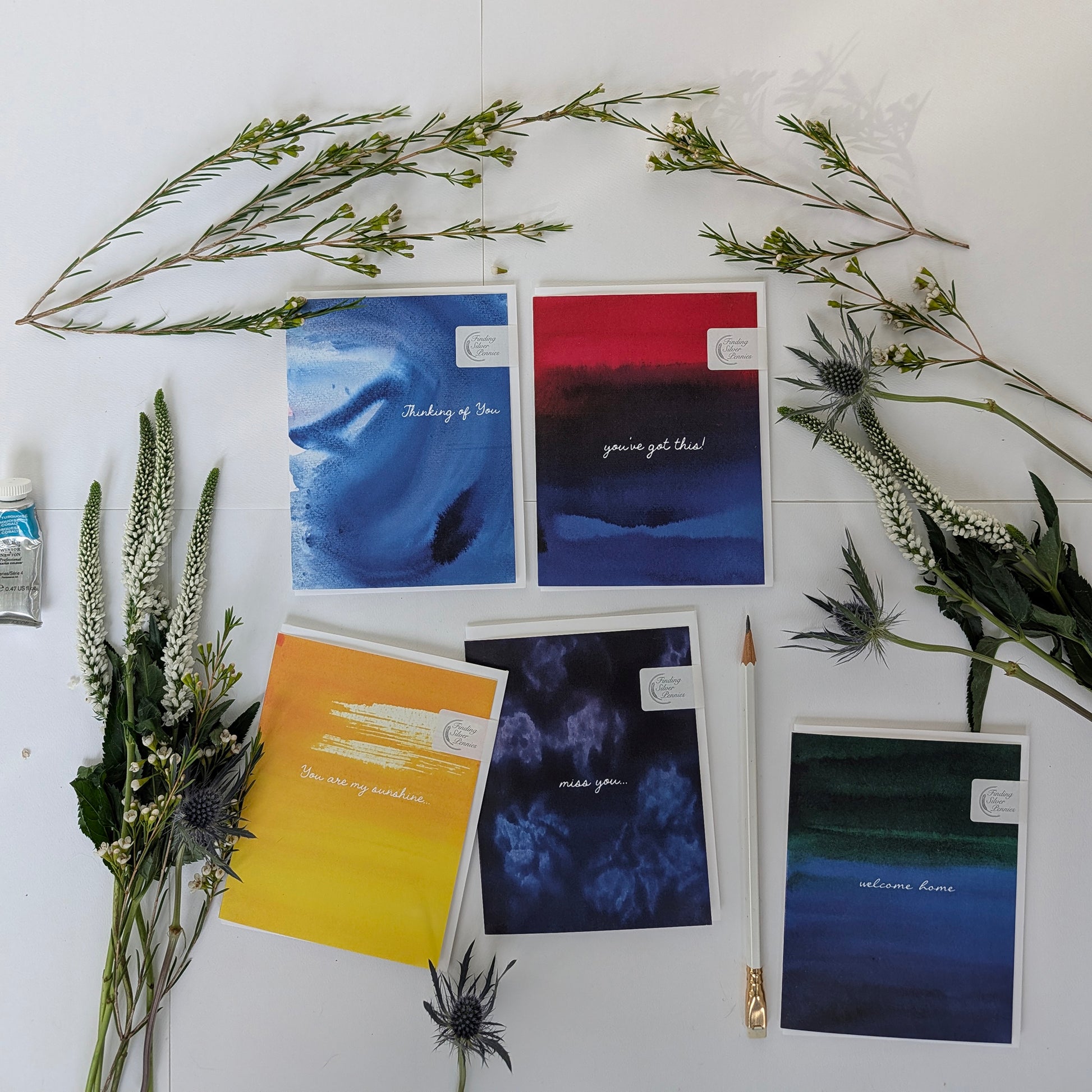 Collection of greeting cards with color washes and text with floral decorations on a white surface