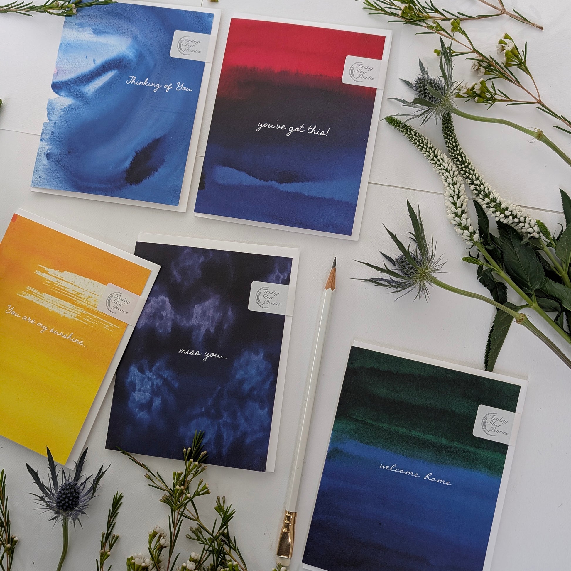 Collection of greeting cards with messages on a white surface with greenery.