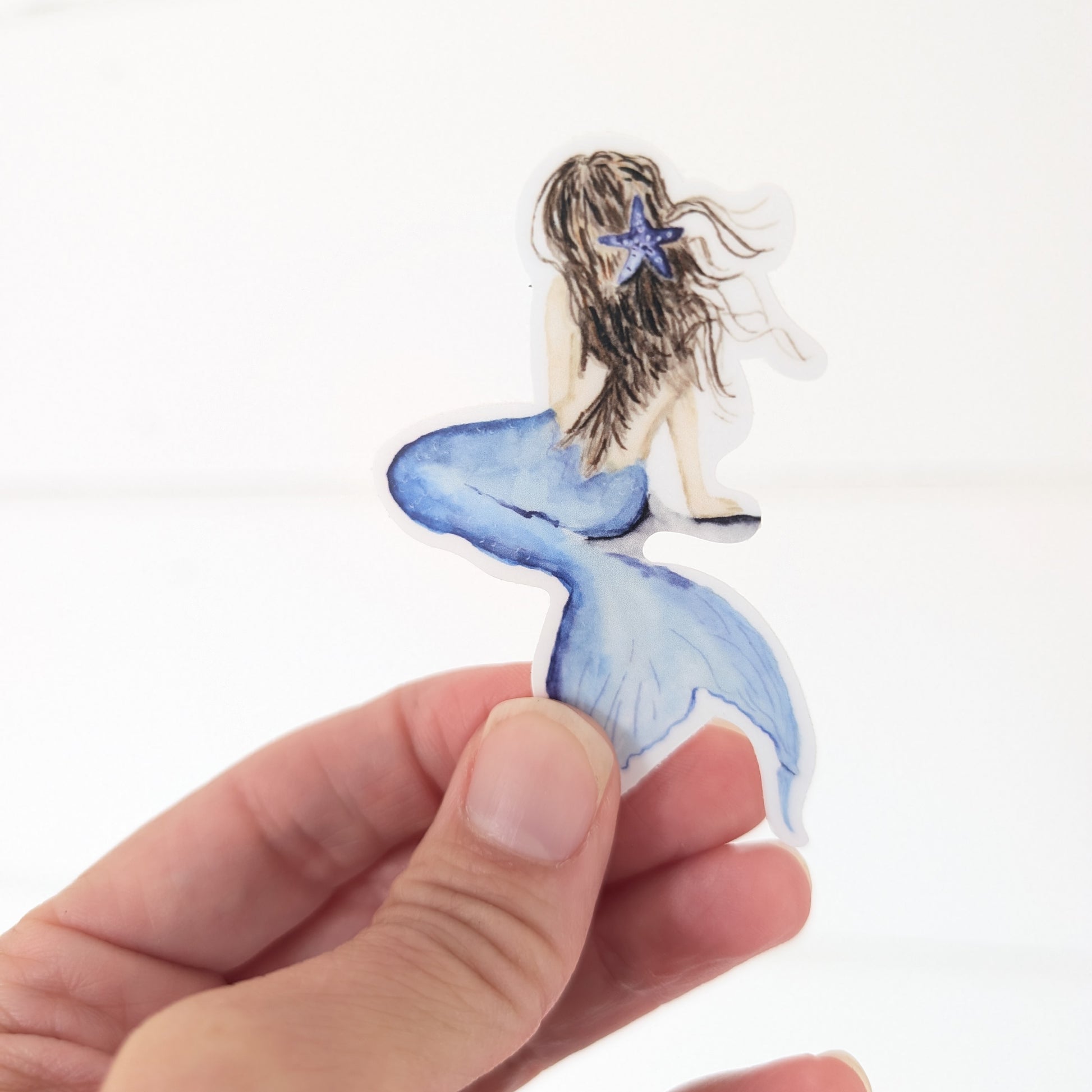 Hand holding a sticker of a mermaid with a blue tail and starfish.