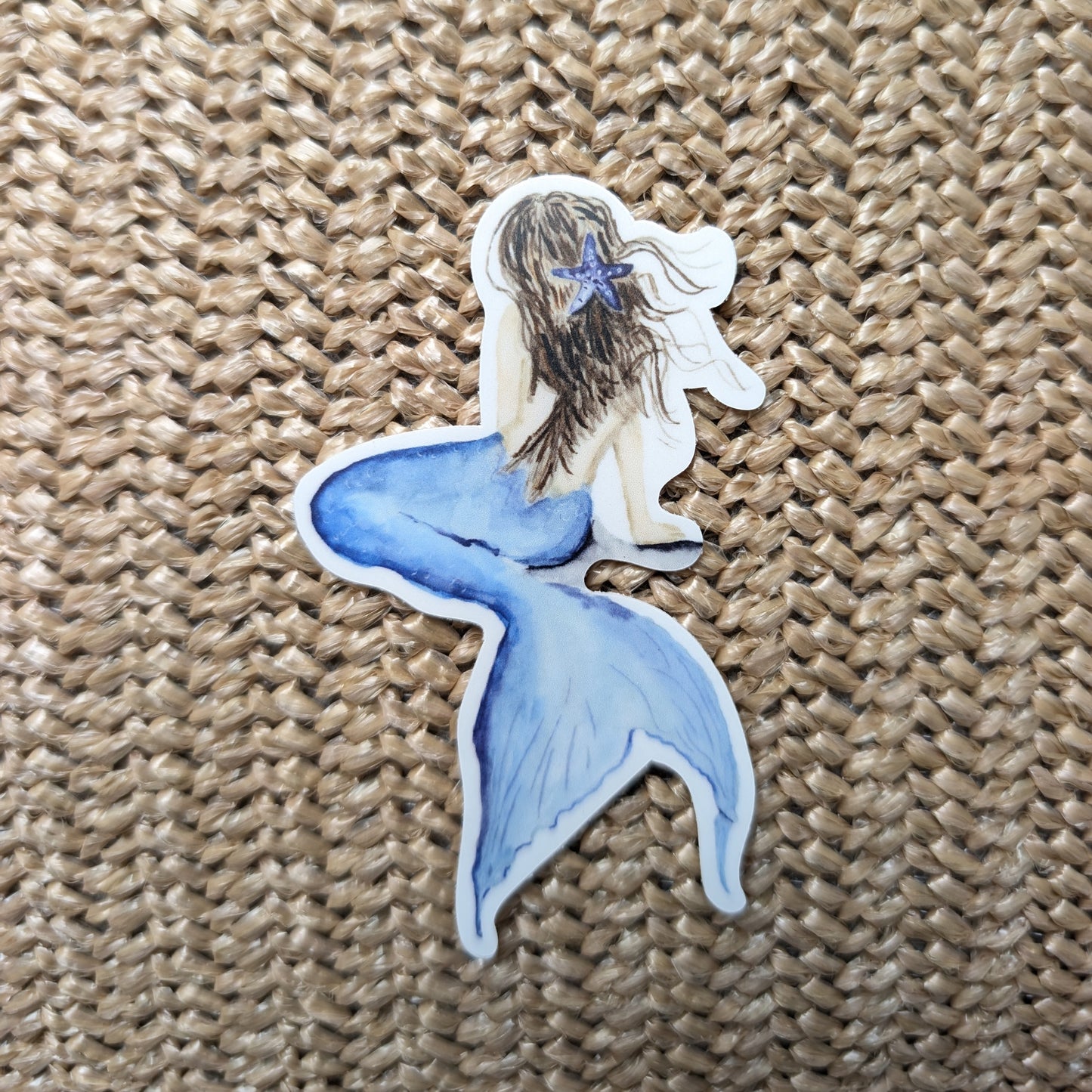 Mermaid sticker with a blue tail and starfish on a textured brown background
