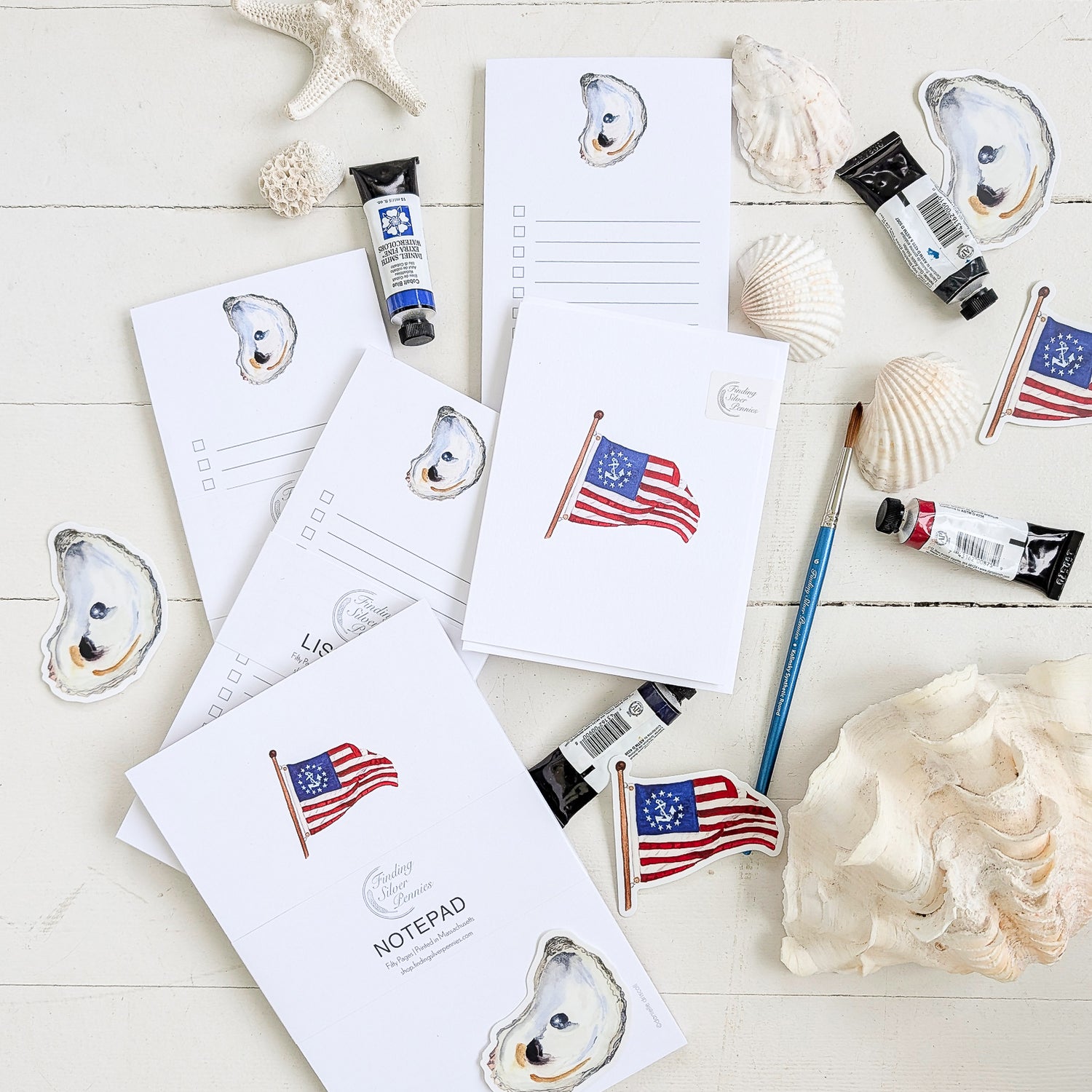 Notepads with oyster designs and American flags on a white surface with art supplies.