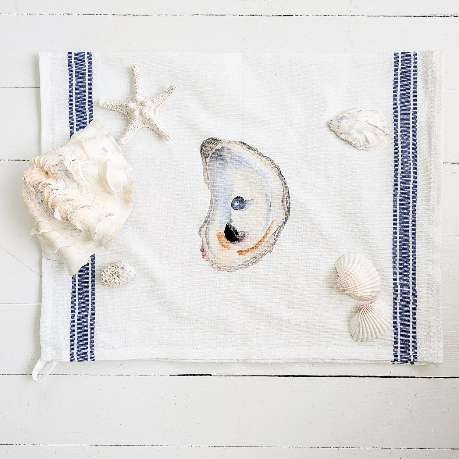 Seashells and a starfish on a white towel with blue stripes on a wooden surface