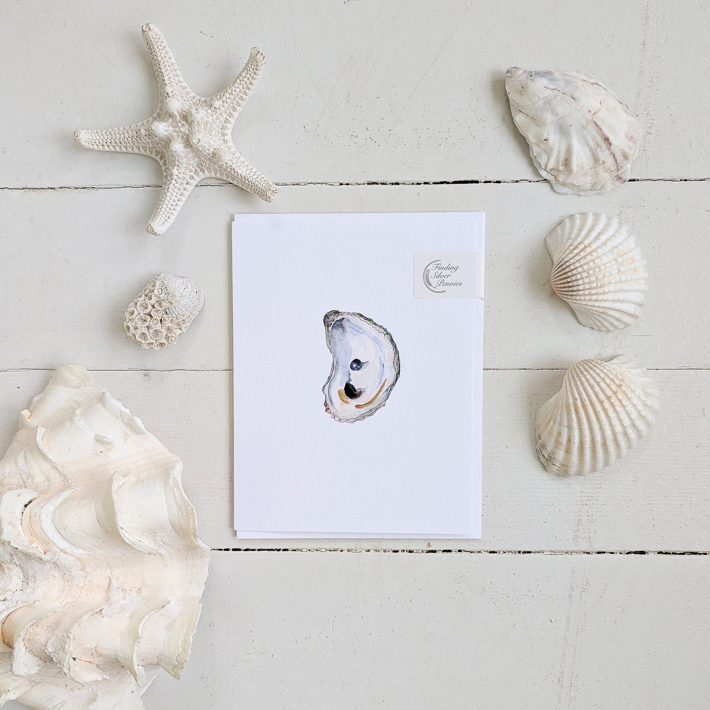 Card with an oyster illustration surrounded by seashells and a starfish on a light wooden surface.