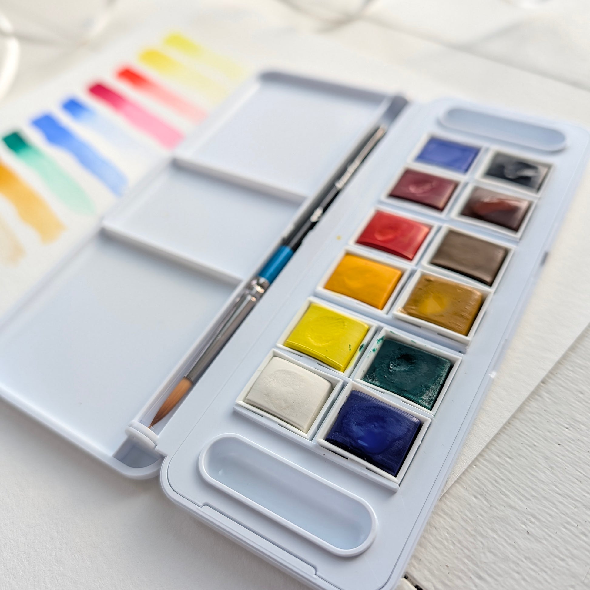 Watercolor paint set with a brush on a light wooden surface