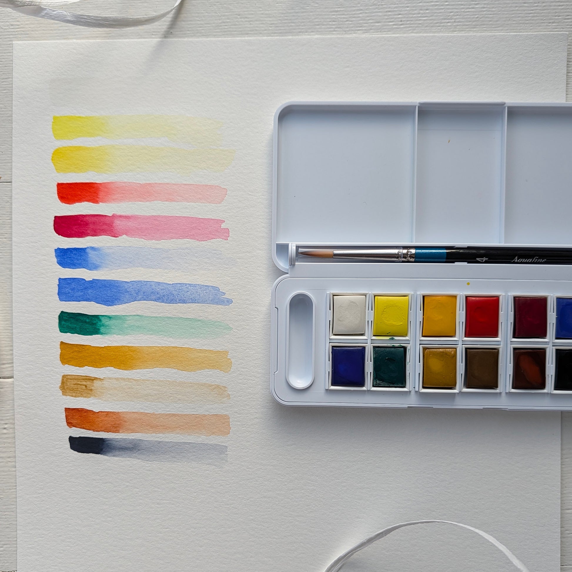 Watercolor swatches on paper with a watercolor palette and brush