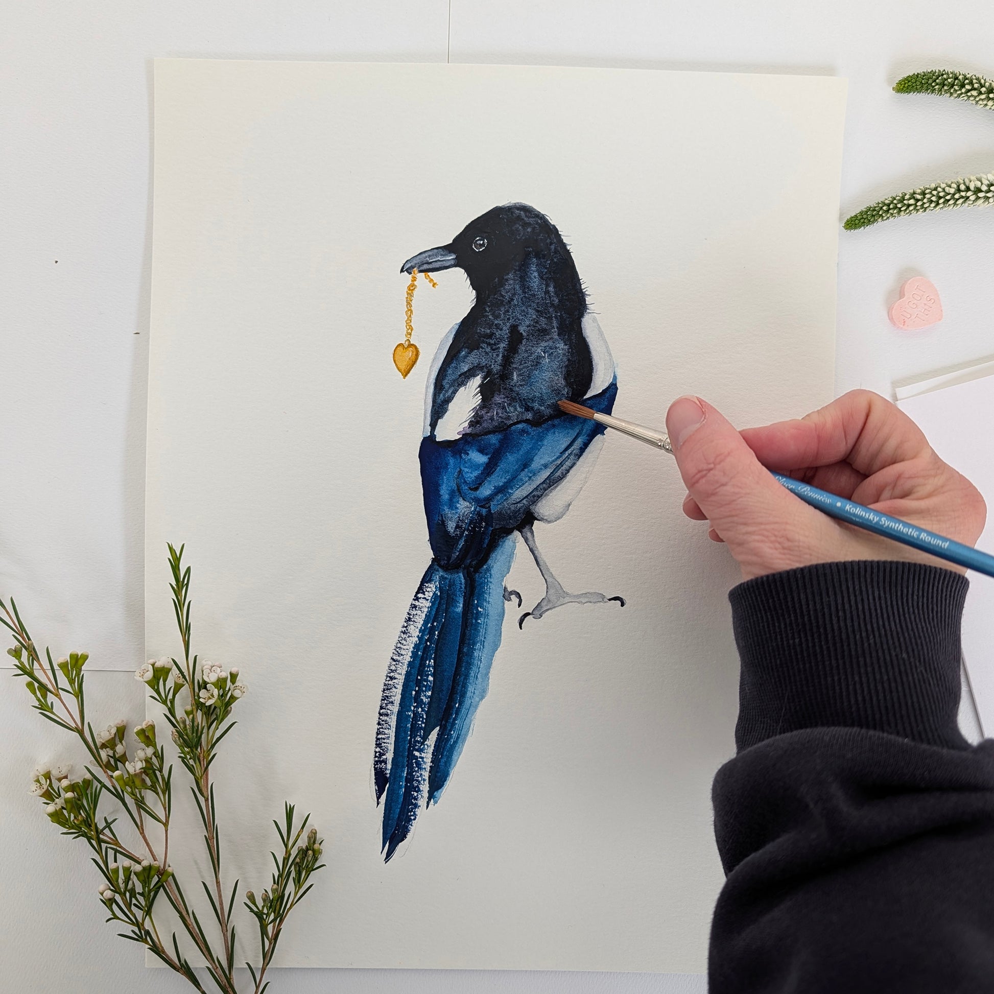 Hand painting a detailed illustration of a magpie on watercolor paper with a white background.