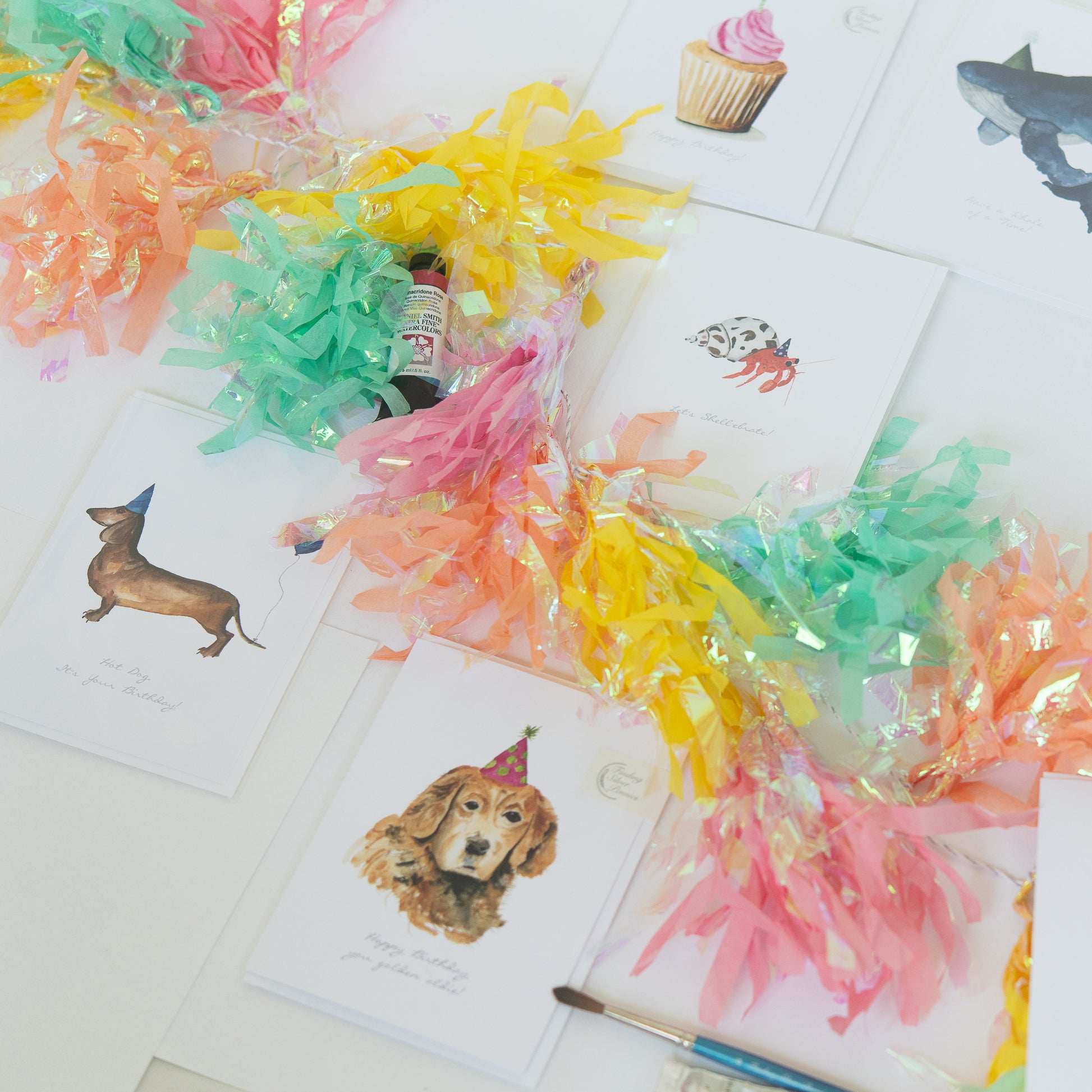 Colorful art supplies on a table with birthday cards featuring animals.