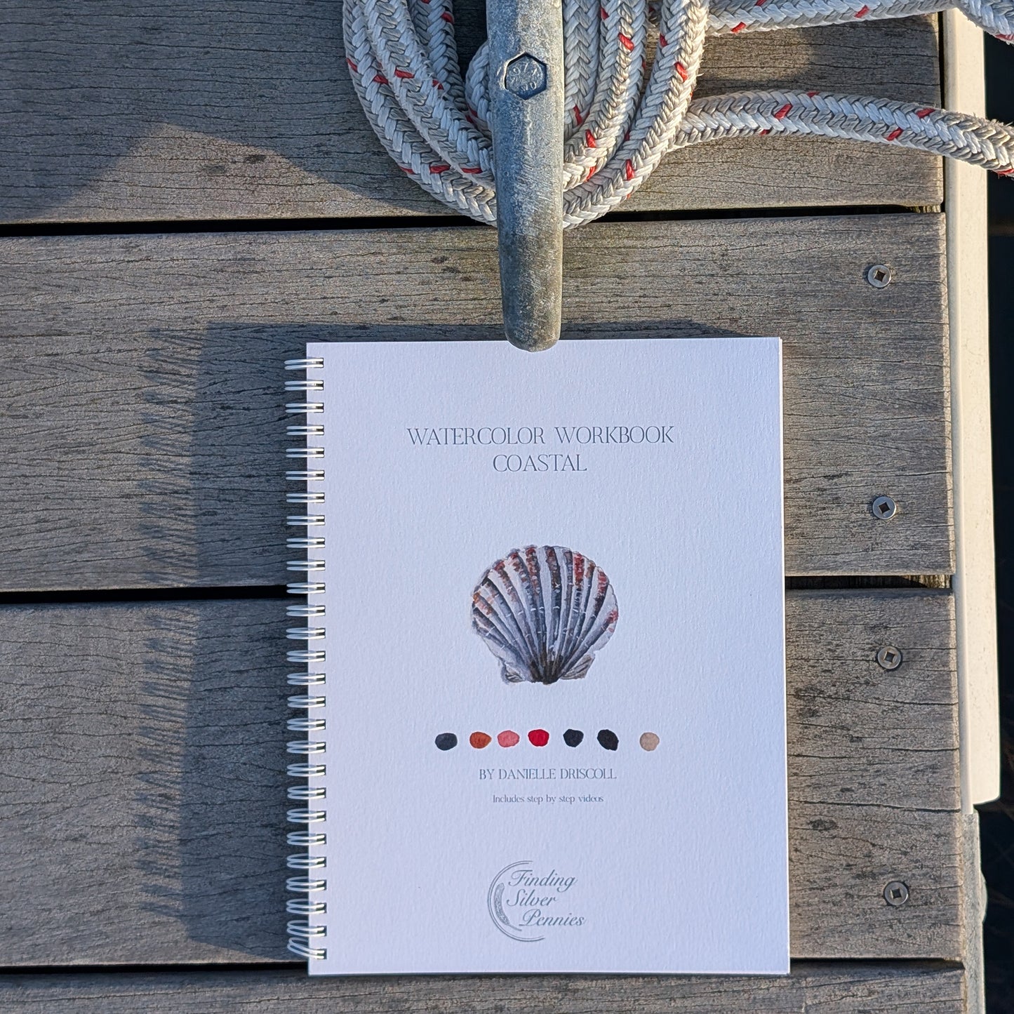 Book titled 'Watercolor Workbook Coastal' with a shell illustration on a wooden surface.