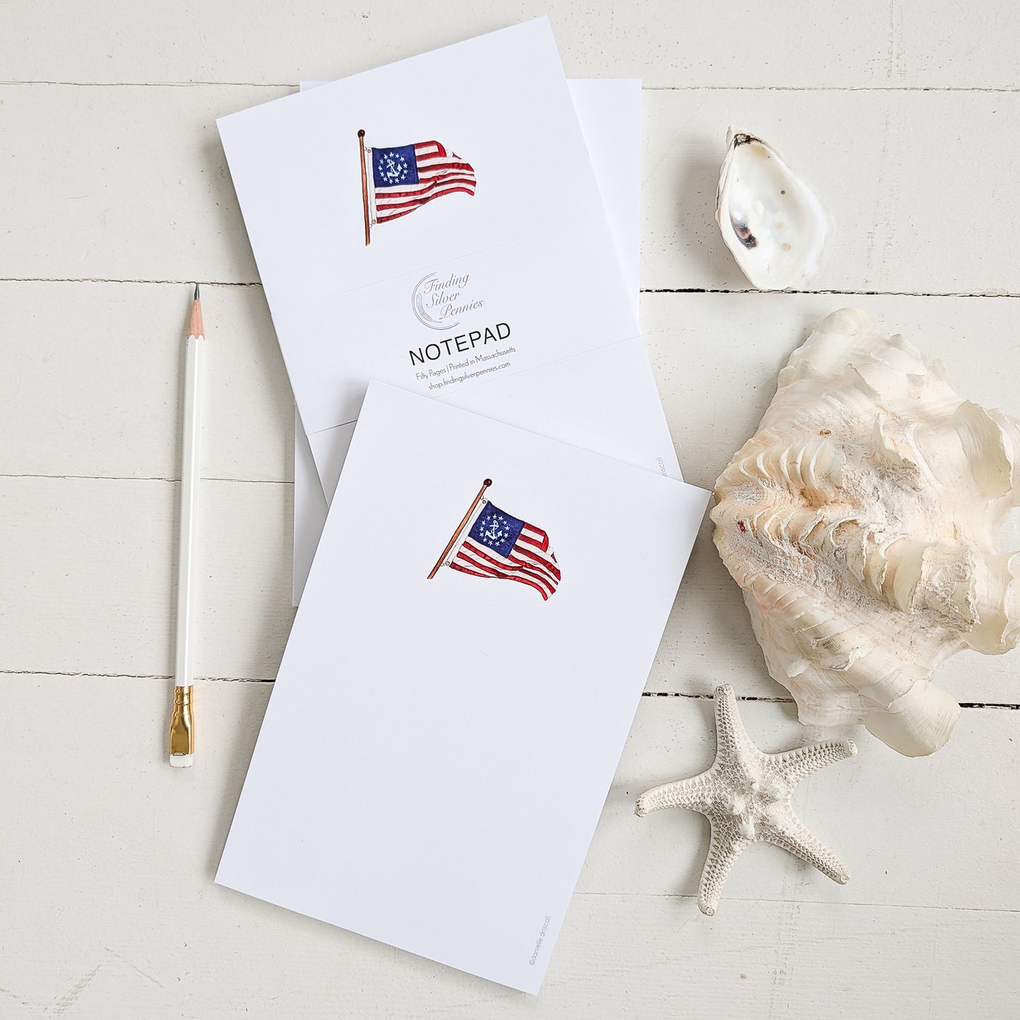 Notepad with American flag (yacht ensign design) on a white surface with a shell and starfish.