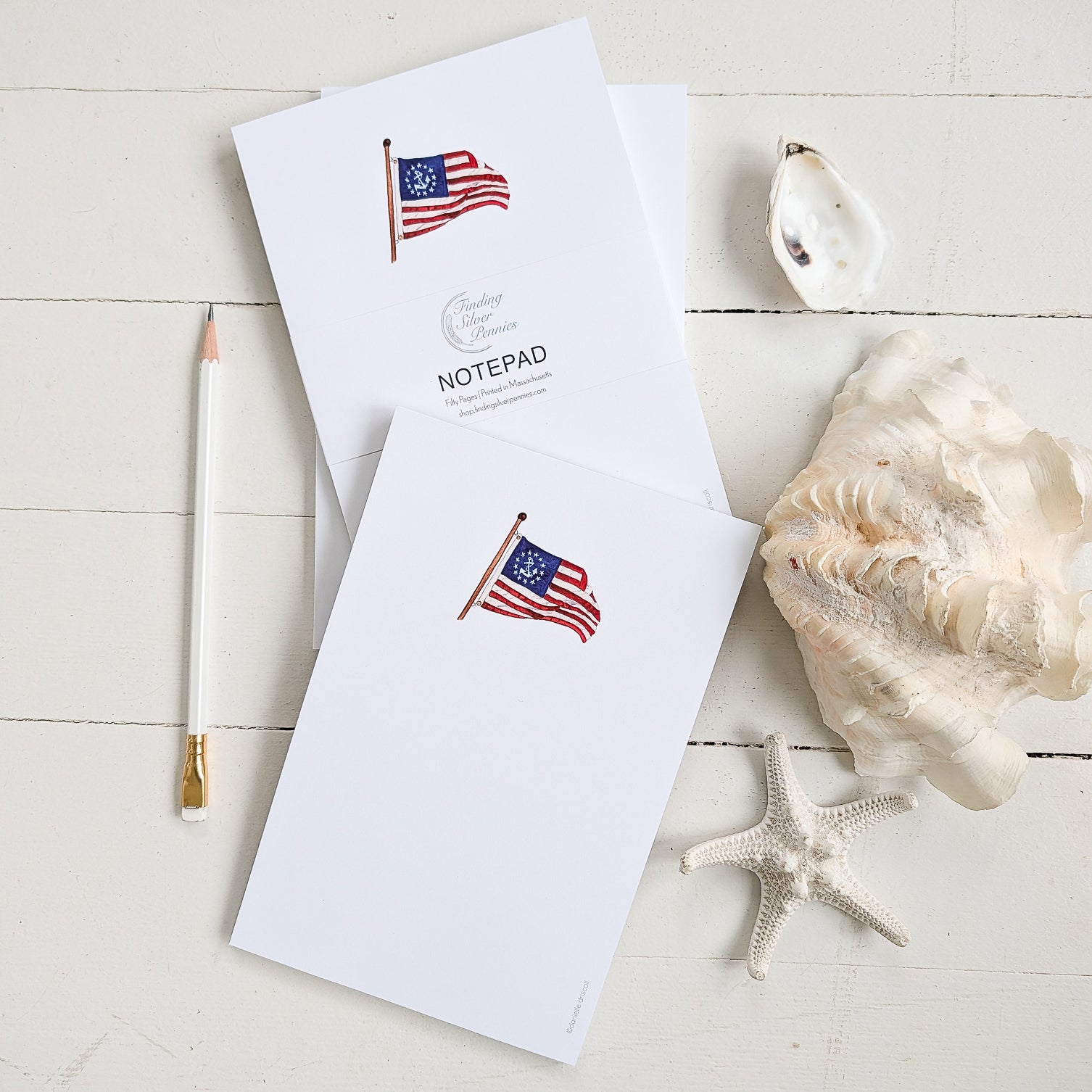 Notepad with American flag (yacht ensign design) on a white surface with a shell and starfish.