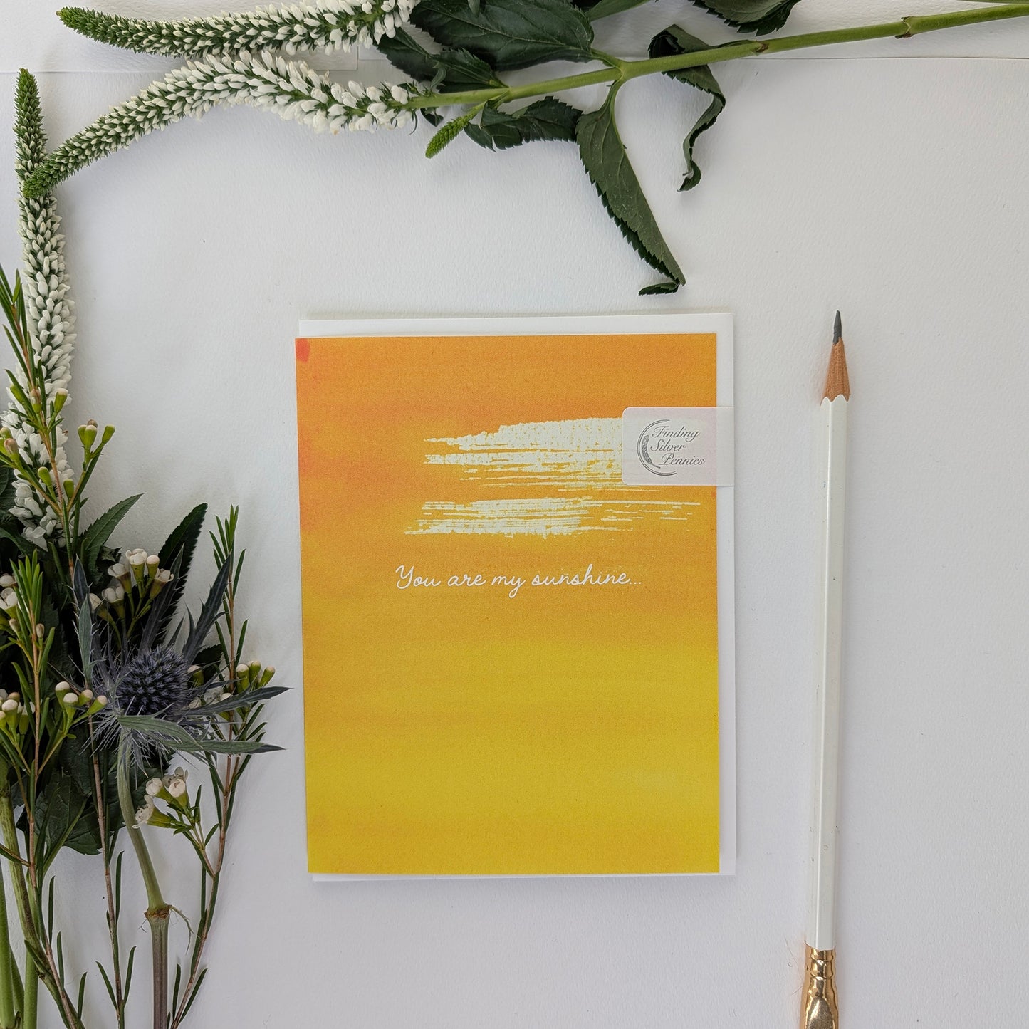 Yellow card with 'You are my sunshine' text, surrounded by flowers and a pencil on a white background