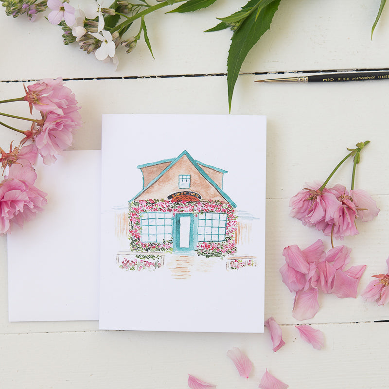 Watercolor Illustration of sweet coastal cafe on a note card with flowers, pencil, and paint brush