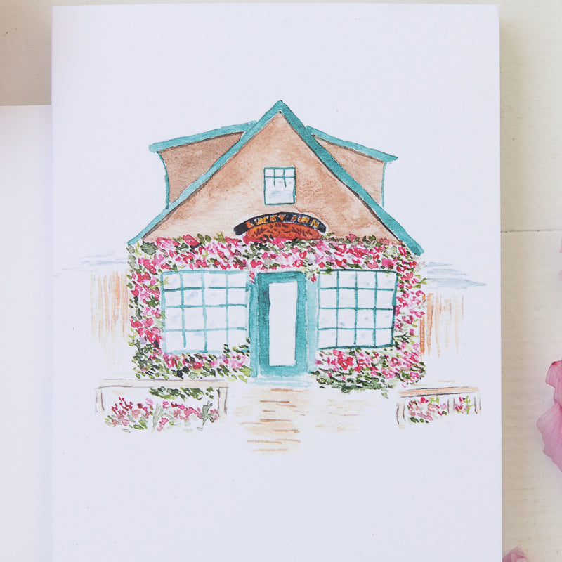 Watercolor Illustration of sweet coastal cafe on a note card with flowers, pencil, and paint brush