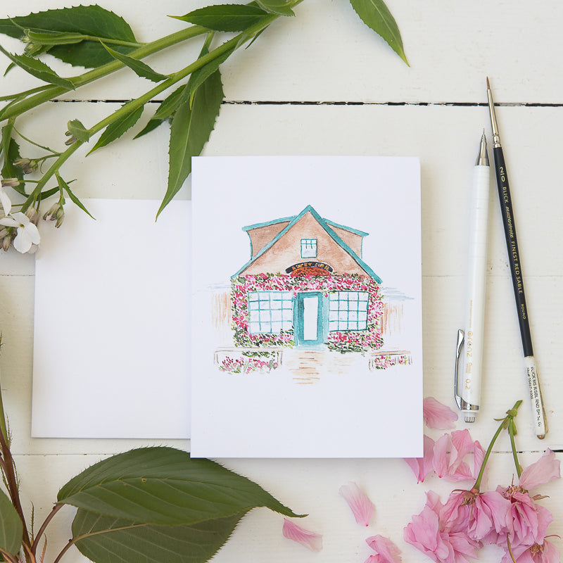 Watercolor Illustration of sweet coastal cafe on a note card with flowers, pencil, and paint brush